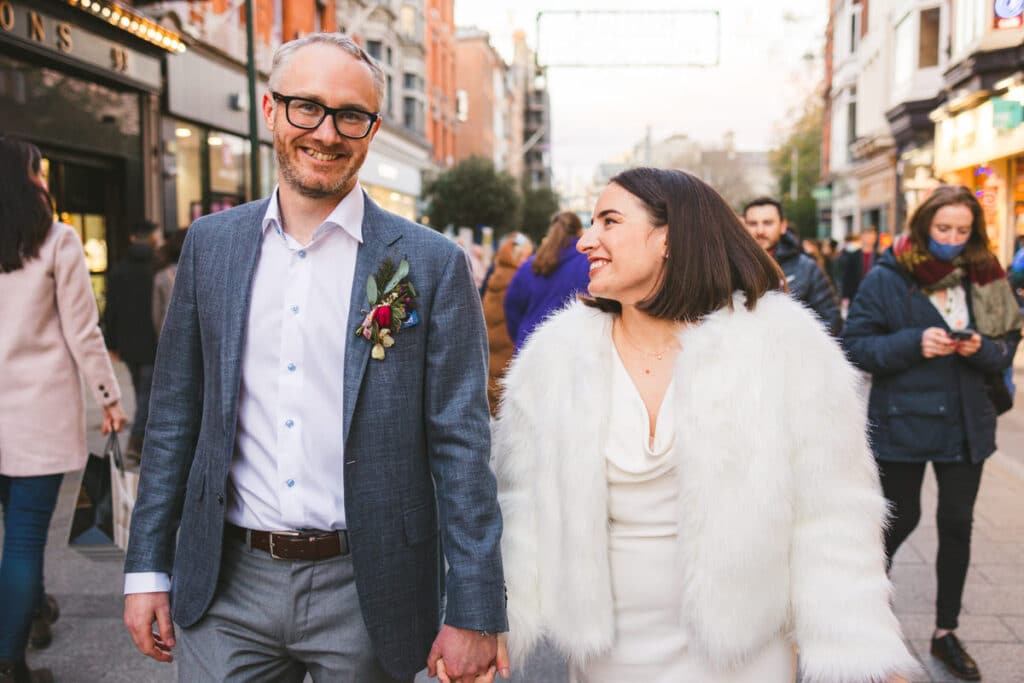Bride wearing fairy jacket walking holding hands Grafton Street wedding photos